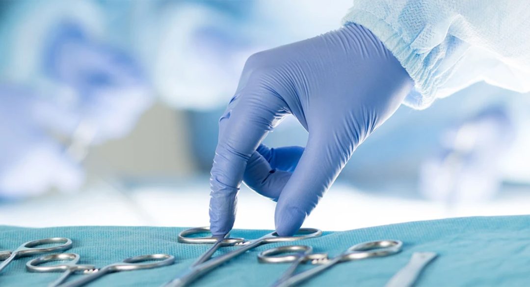 A hand picking up a surgical scissors