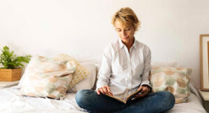 Woman Sitting Cross Legged on Bed Reading Book